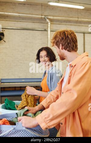 cheerful young asian woman talking to boyfriend near clothes and baskets in coin laundry Stock Photo