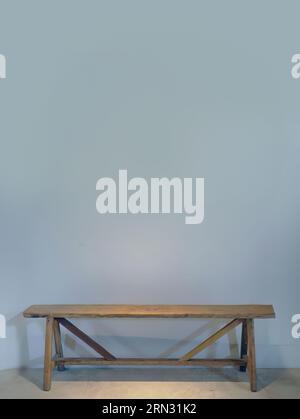 An empty blue grey color wall with a wooden bench against the wall, spotted lighting from above, empty space for copy or text insert, graphic resource Stock Photo