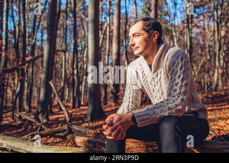 Young handsome man relaxing thinking at peace in autumn forest. Stylish guy enjoying fall landscape wearing warm sweater. Mental health Stock Photo