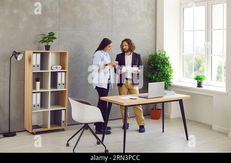 Two business people man and woman standing in office near the workplace and talking. Stock Photo