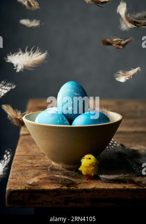 Blue easter eggs in a ceramic bowl. Feathers falling. Easter decorations. Rustic wooden table. Festive easter still life photography. Stock Photo