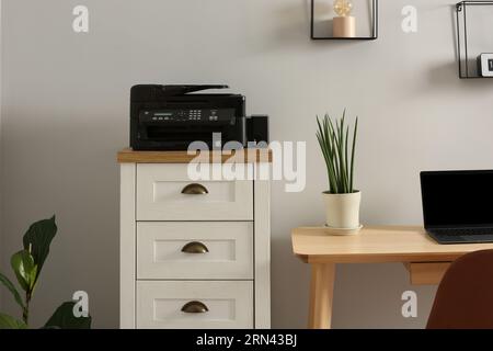 Modern printer on chest of drawers near wooden table indoors Stock Photo