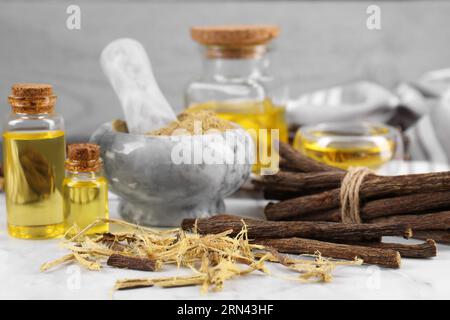 Dried sticks of licorice roots, shavings and essential oil on white table, closeup Stock Photo