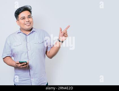 Young latin man holding cellphone pointing to side isolated. Happy guy holding cellphone pointing to the side isolated Stock Photo