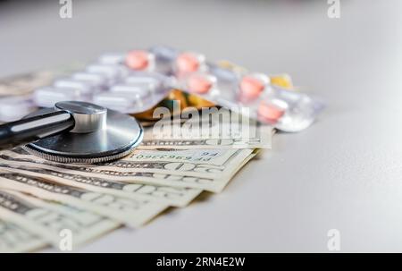 Stethoscope with medicaments on dollar bills. High cost of medical health with stethoscope. Close up of stethoscope with pills on dollar bills Stock Photo