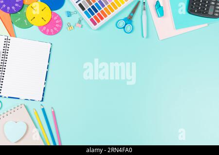 Back to school background. Colored pencils, books, notebooks, pens, watercolor paint, scissors, math fractions, calculator on pastel green background Stock Photo