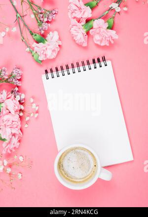 Overhead view coffee cup blank notepad with carnations gypsophila (limonium) flowers pink background Stock Photo