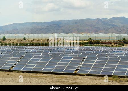 Technologies for obtaining solar energy. Solar panels of the power plant against the backdrop of greenhouses and mountains. Stock Photo