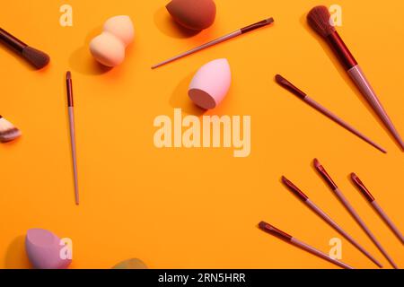 Frame made of makeup sponges and brushes on orange background Stock Photo