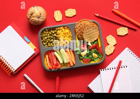 Lunchbox with delicious food and different stationery on red background Stock Photo
