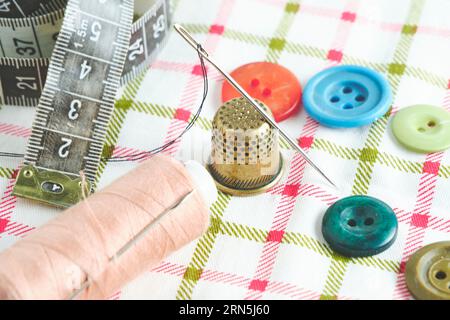 Sewing kit consisting needle, thimble, threads and measuring meter on a fabric background Stock Photo
