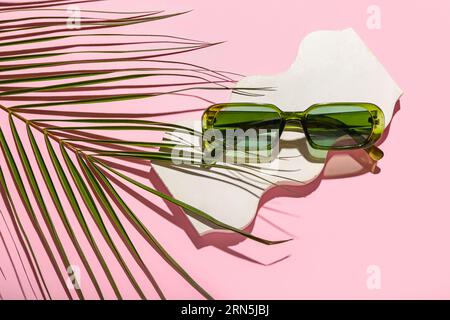 Decorative podium with stylish sunglasses and palm leaf on pink background Stock Photo