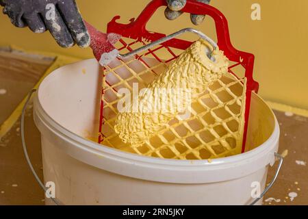 Paint roller on scraper grid in bucket with wall paint, painting work Stock Photo