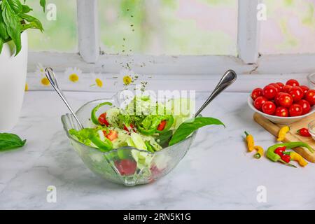 Chives fall on mixed salad in glass bowl, tomatoes and pepperoni in background Stock Photo