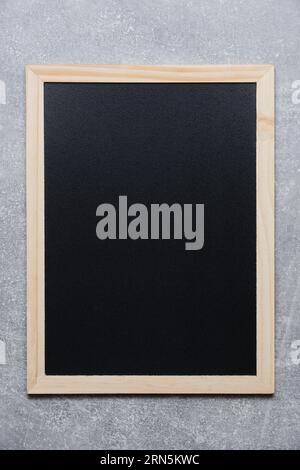 Black chalkboard for notes in wooden frame against gray concrete wall Stock Photo