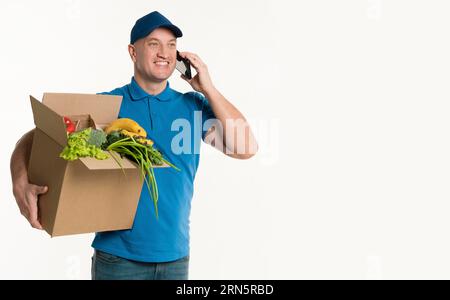 Happy delivery man talking phone holding grocery box Stock Photo