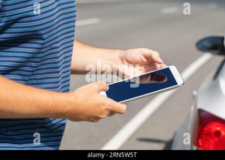 A man with a tablet on the road near the car, a concept on the topic of finding a possible malfunction on the road Stock Photo