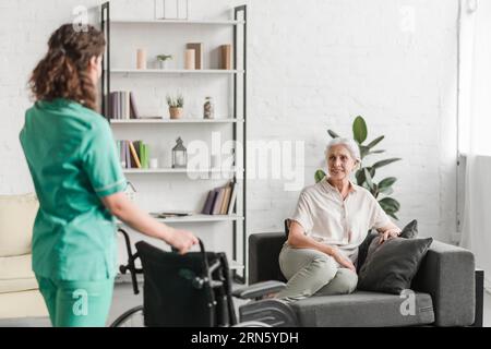 Nurse bringing wheelchair her senor female patient sitting couch Stock Photo