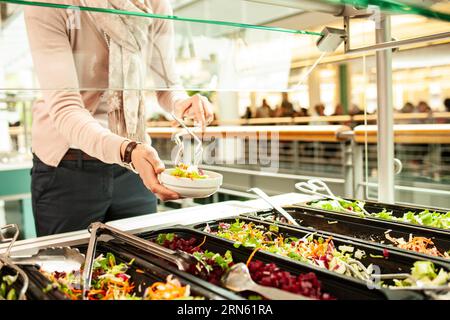 Fresh salads in a salad bar, a woman serves herself at the buffet Stock Photo