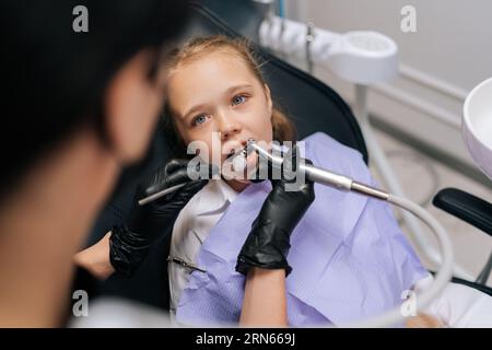 Close-up top view of unrecognizable female orthodontist examining teeth of cute little child girl with dental equipment instrument in dentistry clinic Stock Photo