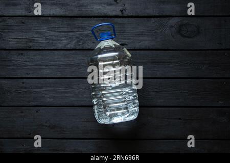 A five-liter plastic water bottle lies on a black wooden board, bottled water Stock Photo