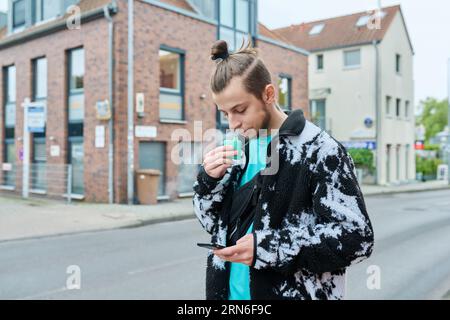 Young hipster male using smartphone, smoking disposable electronic cigarette Stock Photo