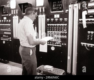 1970s MAN READING A REPORT STANDING BEFORE A COMPLEX CONTROL PANEL IN A CHEMICAL COMPANY - i6434 HAR001 HARS PROFESSION MIDDLE-AGED B&W PANEL MIDDLE-AGED MAN DATA SKILL BEFORE OCCUPATION SKILLS CHEMICAL CAREERS MONITORS LABOR EMPLOYMENT OCCUPATIONS CONCEPTUAL COMPANY COMPLEX CONTROLS MONITORING EMPLOYEE READINGS BLACK AND WHITE CAUCASIAN ETHNICITY COMPUTING HAR001 LABORING OLD FASHIONED Stock Photo