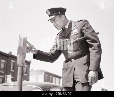 1960s AFRICAN-AMERICAN POLICEMAN IN UNIFORM CHECKING A PARKING METER - p7069 HAR001 HARS UNIFORMS OFFICERS POLICEMEN COPS YOUNG ADULT MAN BADGE BADGES BLACK AND WHITE HAR001 OLD FASHIONED AFRICAN AMERICANS Stock Photo