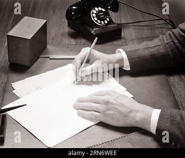 1940s man’s hands writing on blank paper with pencil at desk with telephone - s9455 HAR001 HARS ON AUTHORITY EMPLOYMENT OCCUPATIONS PHONES CONCEPT CONCEPTUAL TELEPHONES MAN'S EMPLOYEE SYMBOLIC CONCEPTS BLACK AND WHITE CAUCASIAN ETHNICITY HANDS ONLY HAR001 OLD FASHIONED REPRESENTATION Stock Photo