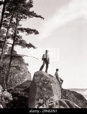 1930s MAN AND WOMAN STANDING ON TOP OF LARGE BOULDERS LAKE OF THE WOODS ONTARIO CANADA - c6033 HAR001 HARS HEALTHY BALANCE TEAMWORK VACATION ATHLETE JOY LIFESTYLE FEMALES MARRIED RURAL SPOUSE HUSBANDS NATURE COPY SPACE FULL-LENGTH LADIES PERSONS SCENIC INSPIRATION MALES RISK ATHLETIC CONFIDENCE B&W ONTARIO PARTNER GOALS SUCCESS TIME OFF VISION ACTIVITY PHYSICAL ADVENTURE STRENGTH TRIP AND GETAWAY EXCITEMENT RECREATION OPPORTUNITY HOLIDAYS CONCEPTUAL ESCAPE EXTREME FLEXIBILITY MUSCLES STYLISH ROCK CLIMBING MID-ADULT MID-ADULT MAN MID-ADULT WOMAN RELAXATION TOGETHERNESS VACATIONS WIVES Stock Photo