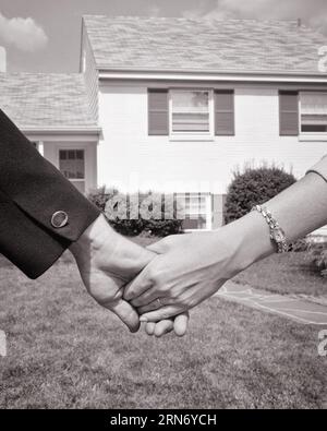 1960s MAN WOMAN HOLDING HANDS IN FRONT OF SUBURBAN SPLIT-LEVEL HOUSE COUPLE HUSBAND & WIFE HOME OWNERS BUYERS - s14880 HAR001 HARS HUSBANDS GROWNUP HOME LIFE COPY SPACE FRIENDSHIP LADIES PERSONS RESIDENTIAL GROWN-UP CARING MALES BUILDINGS B&W PARTNER GOALS SUCCESS DREAMS MANUAL EXTERIOR PRIDE HOLDING HANDS HOMES BUYERS CONNECTION CONCEPTUAL HOMEOWNER RESIDENCE OWNERS MAN & WOMAN SYMBOLIC MID-ADULT MID-ADULT MAN MID-ADULT WOMAN TOGETHERNESS WIVES BLACK AND WHITE CAUCASIAN ETHNICITY HAR001 OLD FASHIONED Stock Photo
