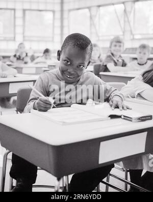 1960s SMILING AFRICAN AMERICAN BOY ELEMENTARY GRADE SCHOOL STUDENT SITTING AT HIS DESK IN CLASSROOM WRITING IN WORKBOOK - s15750 HAR001 HARS FULL-LENGTH INSPIRATION CARING MALES CONFIDENCE B&W EYE CONTACT GOALS SCHOOLS SUCCESS DREAMS GRADE HAPPINESS HEAD AND SHOULDERS CHEERFUL DISCOVERY HIS AFRICAN-AMERICANS AFRICAN-AMERICAN EXCITEMENT PROGRESS BLACK ETHNICITY PRIDE IN OPPORTUNITY PRIMARY SMILES CONNECTION CONCEPTUAL JOYFUL STYLISH GRADE SCHOOL GROWTH JUVENILES BLACK AND WHITE HAR001 OLD FASHIONED AFRICAN AMERICANS Stock Photo
