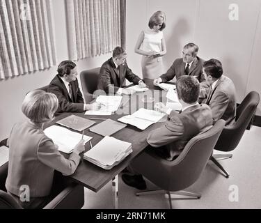 1960s 1970s CONFERENCE IN BOARD ROOM 5 MEN ONE WOMAN SEATED AT TABLE IN DISCUSSION WITH FEMALE SECRETARY STANDING TAKING NOTES - o2655 HAR001 HARS INFORMATION ASSISTANT LIFESTYLE CLERK FEMALES 5 DECISION MANAGER SEATED COPY SPACE HALF-LENGTH LADIES PERSONS MALES CORPORATE PROFESSION EXECUTIVES B&W BUSINESSWOMAN GOALS OCCUPATION HIGH ANGLE STRATEGY CAREERS LEADERSHIP SEVEN MAKERS OFFICE WORKER OPPORTUNITY OCCUPATIONS BOSSES GAL FRIDAY 7 ADMINISTRATOR SECRETARIES STYLISH SUPPORT BUSINESSWOMEN AMANUENSIS COOPERATION DIRECTORS IDEAS MANAGERS SOLUTIONS TOGETHERNESS BLACK AND WHITE Stock Photo