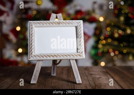 Small easel with framed blank postcard on wooden table with Christmas background. Mockup of Christmas card. Stock Photo