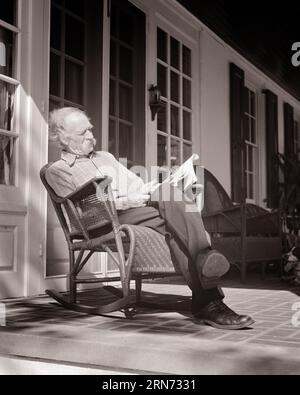 1940s SENIOR MAN READING NEWSPAPER SITTING IN ROCKING CHAIR ON PORCH - s9704 HAR001 HARS FREEDOM MUSTACHE RETIREE HAPPINESS OLDSTERS OLDSTER LEISURE MUSTACHES ROCKING CHAIR FACIAL HAIR ELDERS ELDERLY MAN RELAXATION BLACK AND WHITE CAUCASIAN ETHNICITY HAR001 OLD FASHIONED Stock Photo