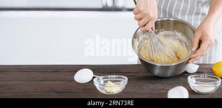 A cook in an apron kneads the dough in a bowl using a whisk for baking bread, dessert, pie, buns. Homemade or handmade bread, dessert. Kitchen backgro Stock Photo