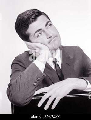 1960s SALESMAN RESTING HEAD AND HANDS ON HIS BRIEFCASE WITH A DISCOURAGED DISPIRITED PUZZLED FACIAL EXPRESSION - s16369 HAR001 HARS MOODY COPY SPACE PENSIVE PERSONS THOUGHTFUL MALES EXPRESSIONS TROUBLED B&W CONCERNED PUZZLED RESTING SADNESS SUIT AND TIE DREAMS HUMOROUS SELLING HEAD AND SHOULDERS HIS STRATEGY AND REFLECTIVE THINK COMICAL MOOD OCCUPATIONS REFLECTING PONDER PONDERING CONSIDER LOST IN THOUGHT GLUM COMEDY CONTEMPLATIVE DISCOURAGED MEDITATE DEJECTED DISAPPOINTED LOOKING UP MEDITATIVE MID-ADULT MID-ADULT MAN MISERABLE SALESMEN BLACK AND WHITE CAUCASIAN ETHNICITY CONSIDERING HAR001 Stock Photo