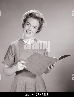 1960s SMILING WOMAN READING FROM FOLDER WEARING HAT DRESS COSTUME JEWELRY NECKLACE PUBLIC SPEAKER CHAIRWOMAN LOOKING AT CAMERA - s4483 HAR001 HARS JEWELRY HALF-LENGTH LADIES PERSONS FOLDER CONFIDENCE B&W LECTURE EYE CONTACT HAPPINESS CHEERFUL AND NETWORKING INSTRUCTOR LEADERSHIP OPPORTUNITY OCCUPATIONS SMILES SPOKESPERSON EDUCATOR JOYFUL STYLISH COSTUME JEWELRY EDUCATING EDUCATORS INSTRUCTORS MID-ADULT MID-ADULT WOMAN PTA SCHOOL TEACHES BLACK AND WHITE CAUCASIAN ETHNICITY HAR001 OLD FASHIONED Stock Photo