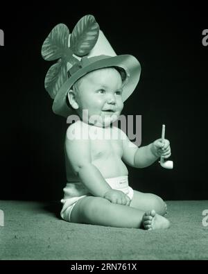 1950s BABY SITTING WEARING ST. PATRICK’S DAY HAT WITH SHAMROCK AND HOLDING CLAY PIPE LOOKING UP SMILING - b5814 HAR001 HARS B&W LUCK SHAMROCK HAPPINESS ST CLAY AND FOLKLORE EXCITEMENT CONCEPTUAL ST. PADDY'S BABY BOY PADDYS PATRICKS GROWTH JUVENILES PATRICK BLACK AND WHITE CAUCASIAN ETHNICITY FEAST DAY HAR001 OLD FASHIONED PATRICK'S Stock Photo
