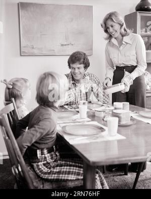 1970s FAMILY OF FOUR READY FOR MEAL SMILING MOTHER SERVING FATHER AND TWO KIDS AT TABLE  - d6154 HAR001 HARS CLOTHING INDOORS NOSTALGIC SERVING PAIR 4 MOTHERS OLD TIME NOSTALGIA BROTHER OLD FASHION SISTER 1 JUVENILE STYLE COMMUNICATION SONS PLEASED FAMILIES JOY LIFESTYLE SATISFACTION FEMALES READY MARRIED BROTHERS SPOUSE HUSBANDS HEALTHINESS HOME LIFE COPY SPACE FRIENDSHIP HALF-LENGTH LADIES DAUGHTERS PERSONS CARING MALES SIBLINGS SISTERS FATHERS B&W PARTNER HAPPINESS CHEERFUL AND DADS SIBLING SMILES SUPPER CONNECTION JOYFUL JUVENILES MEALTIME MID-ADULT MID-ADULT MAN MID-ADULT WOMAN MOMS Stock Photo