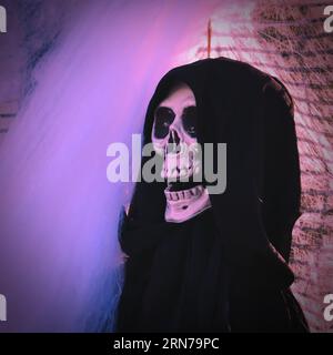 Fun smiling skull skeleton wearing black robe and hood on Halloween Party in neon light Stock Photo