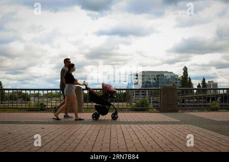 Couple walking with a baby stroller along the Willamette River in Tom McCall Waterfront Park in Downtown Portland Oregon Stock Photo