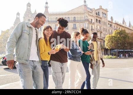 Group smiling multiracial young people using cell phones. Happy fellow university students outdoors. Stock Photo