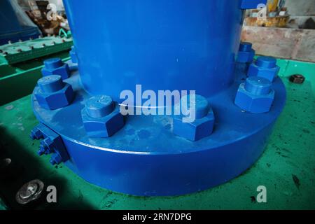 Bolts and nuts on blue flange of joint of hydraulic jack on hydroelectric power plant. Stock Photo