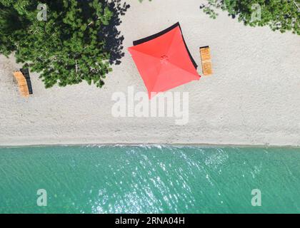 Aerial top view on the beach. Umbrellas, sunbeds, sand and ocean. Aerial view amazing empty white beach with red beach umbrella and turquoise clear wa Stock Photo