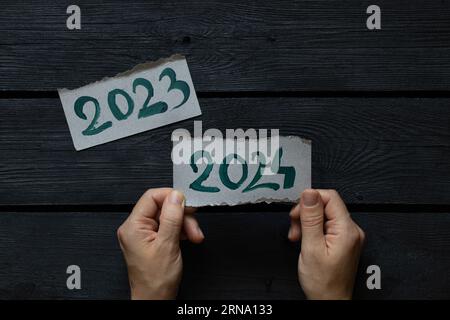 Notepad with the text 2023 and 2024 drawn with paint and a woman's hand turns over the page of the notepad on a black wooden board, the beginning of t Stock Photo