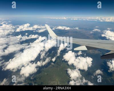White wing from airplane window with mountain range below on sunny day. Great views of desert landscape and snowed peaks from plane Stock Photo