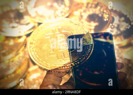 Hand of a person holding a smartphone with golden bitcoins as background concept of Day trader buying selling crypto currency bitcoin concept. Stock Photo