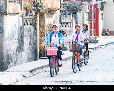 Three young students on bicycles in Hai Thanh, a fishing village along Song Lach Bang River in the Thanh Hoa province of Vietnam. Stock Photo