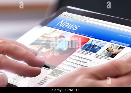 Close-up Of A Person's Hand Using Digital Tablet With Screen Showing Online News Stock Photo